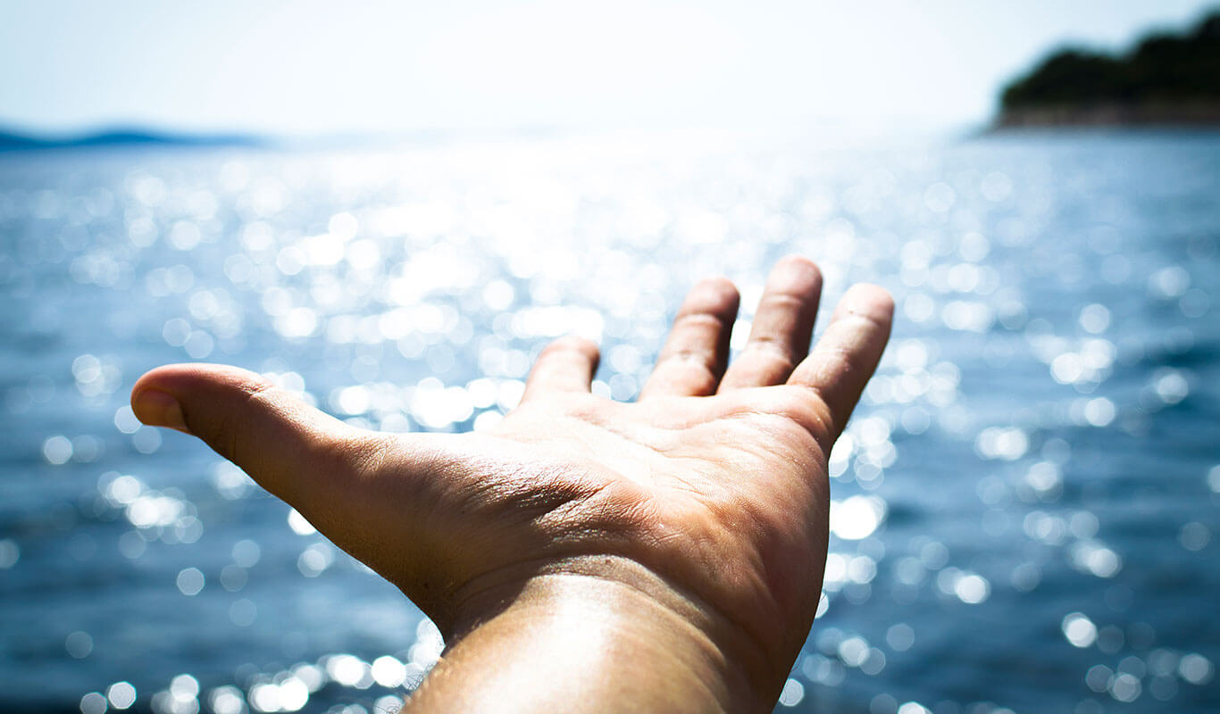 Photo of an outstretched hand against a large body of water